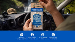 Person holding Fresh Falls scented car air freshener package in vehicle interior with dashboard visible.