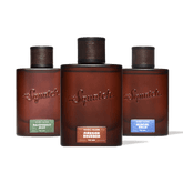 Three Squatch fragrance bottles arranged in a row against a solid green background. The center bottle is upright and labeled 'Squatch Fireside Bourbon', while the left and right bottles are slightly angled backward and labeled 'Squatch Rainforest Mist' and 'Squatch Glacial Falls' respectively.