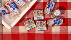 Blue Ribbon Breeze beer bundle displaying three soap bars and multiple cans arranged on red and white checkered cloth.