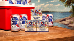 Blue Ribbon Breeze limited edition men's natural soap three-pack boxes displayed with beer cans by a lakeside setting.