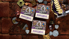 Three boxes of Dr. Squatch Mimic Bricc natural soap surrounded by Dungeons & Dragons dice and metal tokens on a textured brown surface.